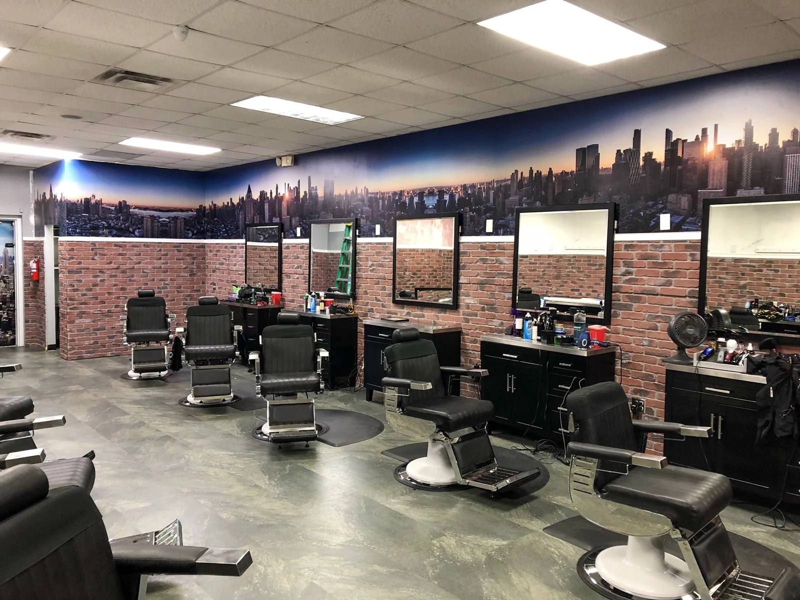 Barbershop interior with a city skyline wall mural above faux brick and rows of barber chairs, Big City Barbers project