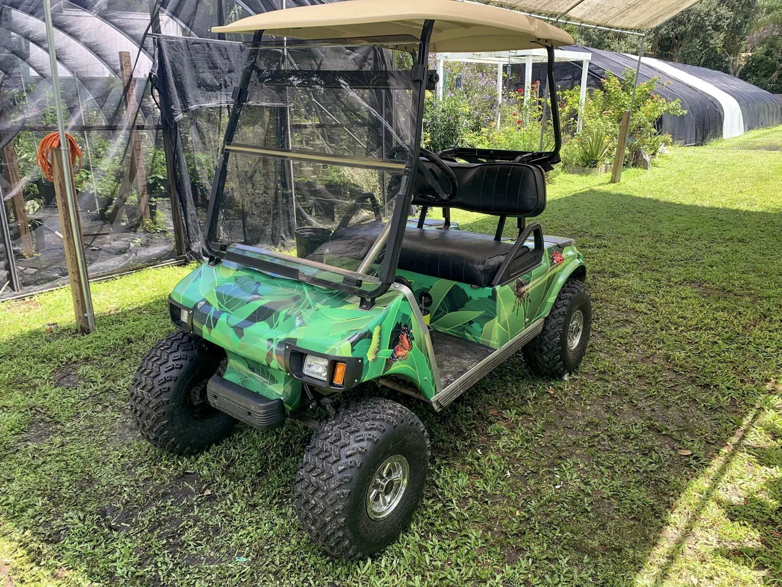 Butterfly Dans — Golf cart with a green camouflage-style wrap beside a garden enclosure, Butterfly Dan's project