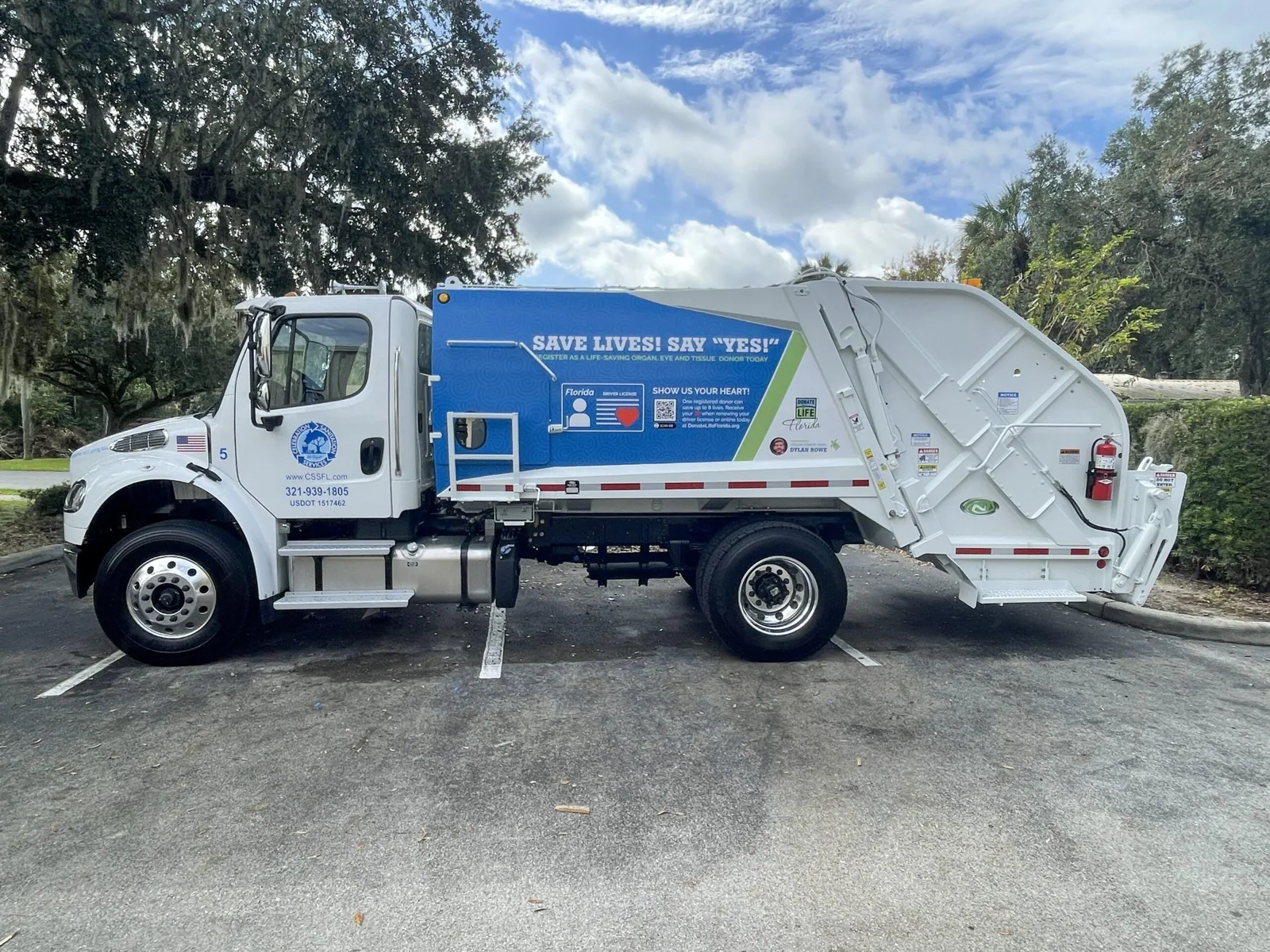 Side view of a garbage truck with a blue Save Lives! Say Yes! wrap on the body, Celebration Sanitation project
