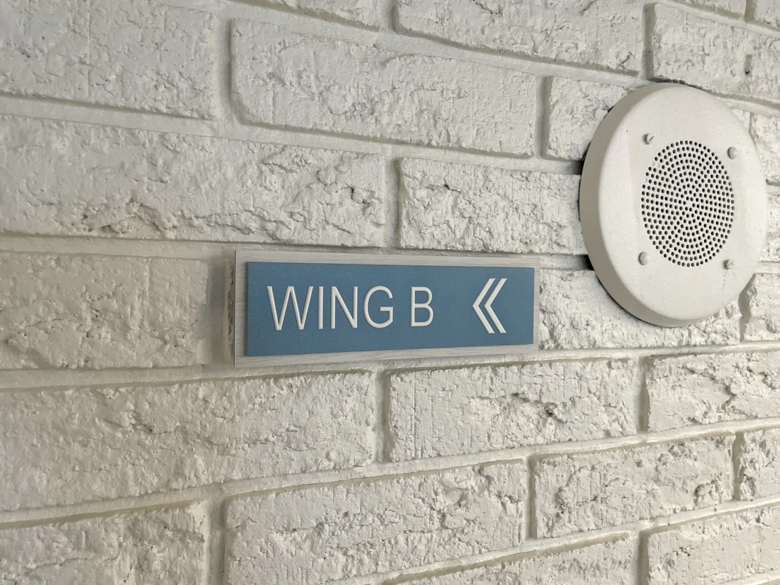 Unisen Senior Living — Wing B directional sign with arrow on a white-painted brick wall, Unisen Senior Living project