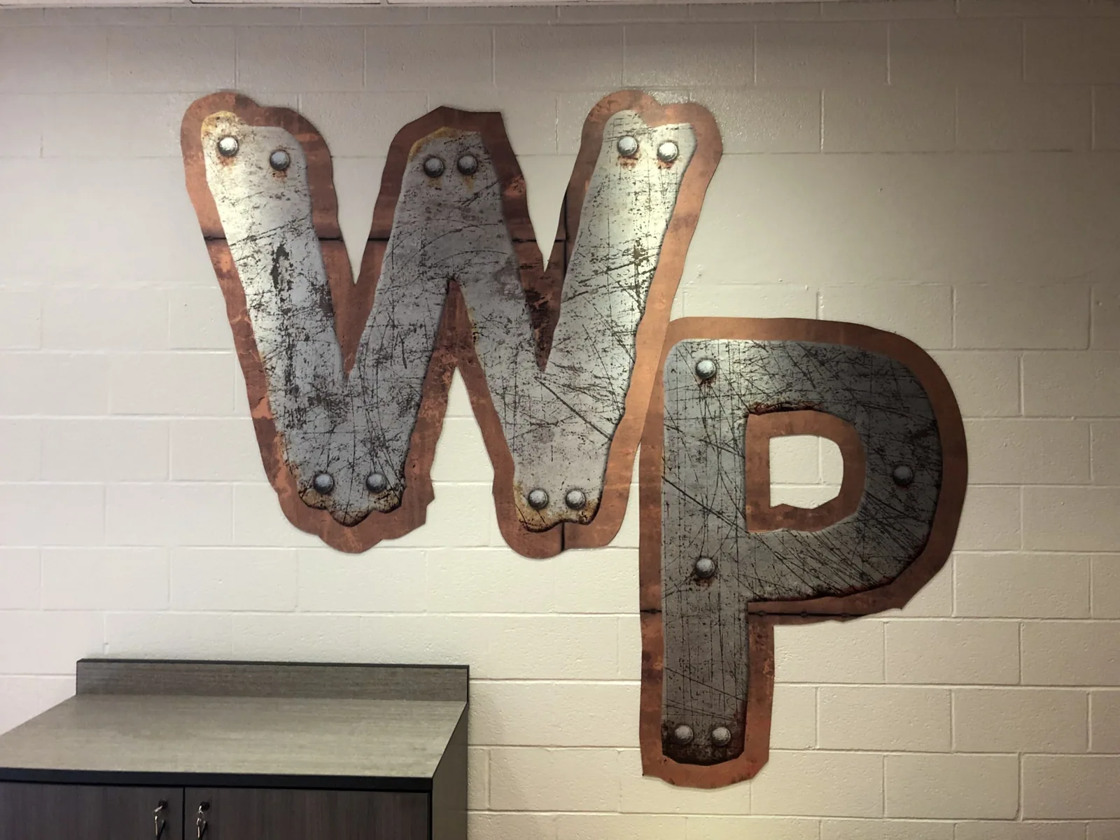 Winter Park High School — Large WP letters with riveted metal-look finish on a white block wall, Winter Park High School project