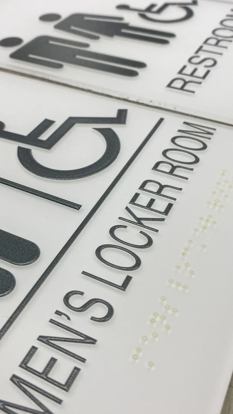 Close-up of restroom and locker room signs with pictograms, raised letters and Braille