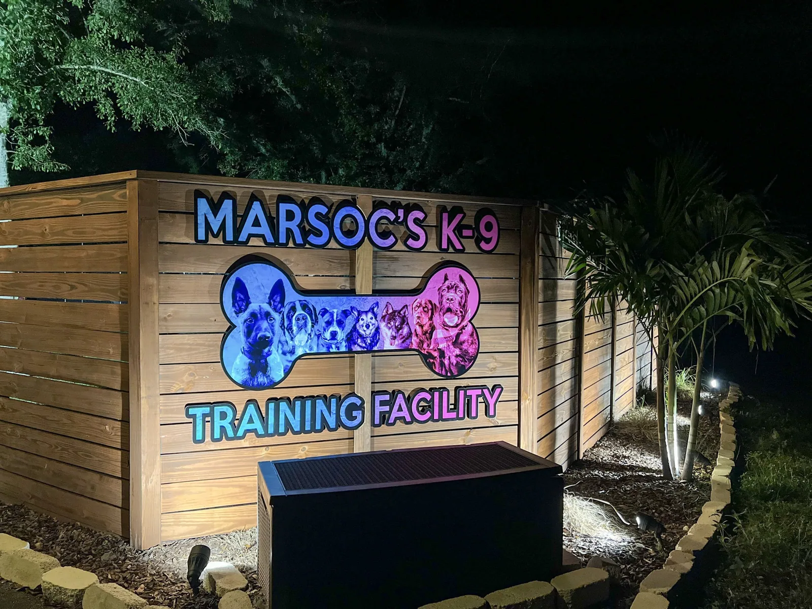 Illuminated MARSOC's K-9 Training Facility sign on a wood fence at night