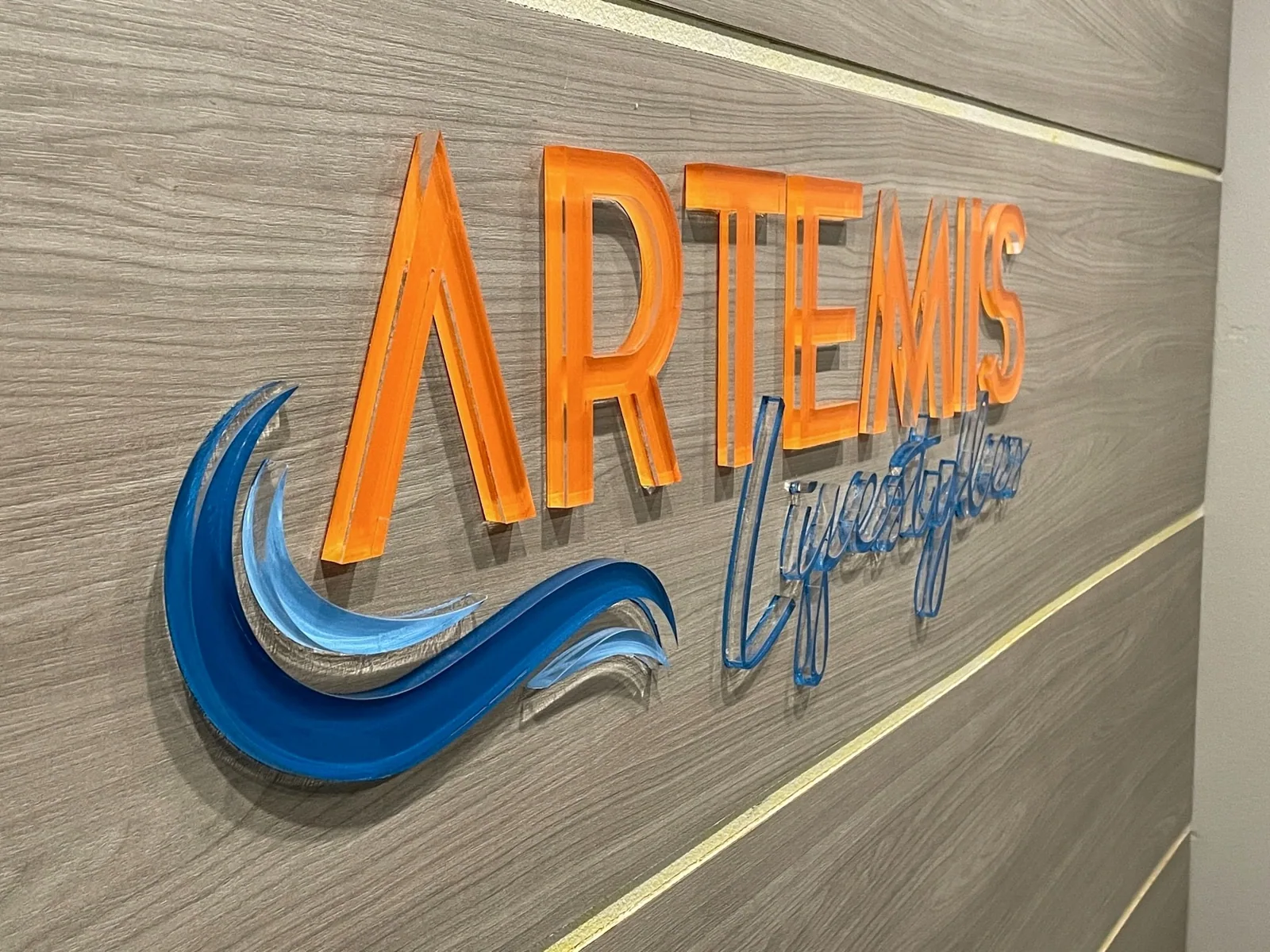 Artemis Lifestyles dimensional acrylic logo on a wood-grain wall