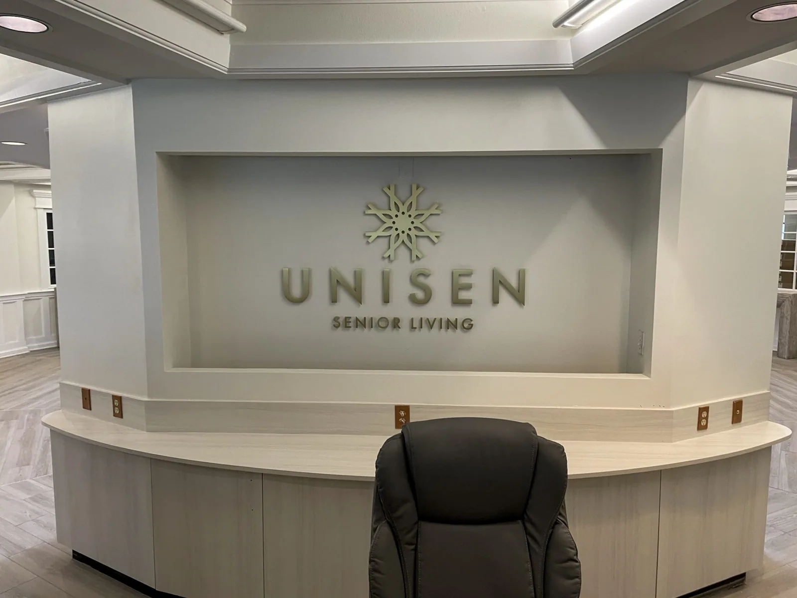Unisen Senior Living dimensional logo in the niche behind a reception desk, Unisen Senior Living project
