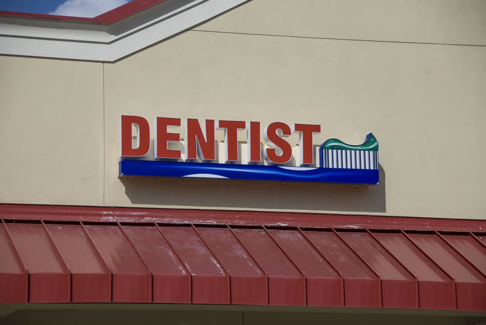 Red DENTIST channel letters with logo above a red metal awning on a storefront